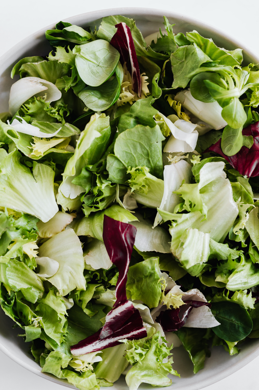 Bowl of greens for a salad that includes vegetables like red cabbage, spinach, lettuce, and kale