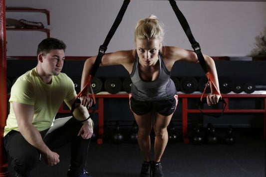 Woman working out her arms and exercising with a male trainer at the gym