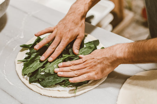 Person making a pesto pizza, focusing on the toppings and kneading the dough