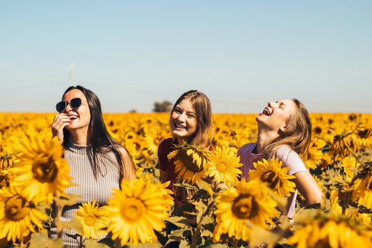 Three girls in a sunflower field smiling and laughing with one another, high levels of serotonin