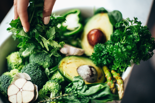 Bowl of a variety of vegetables and plants like avocados, herbs, basil, cilantro, broccoli, peppers, mushrooms, asparagus, spinach