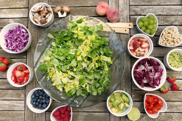 Salad preparation with fruits (strawberries, blueberries, grapes, peaches, tomatoes, raspberries, limes), nuts, and vegetables (lettuce, greens, onions, mushrooms)